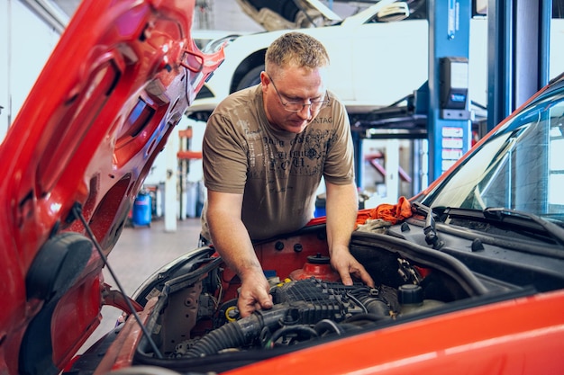 A man with glasses maintains a car in a garage car repair by an experienced specialist in a car repair shop replacing the oil and filter in the car an auto mechanic performs car repairs