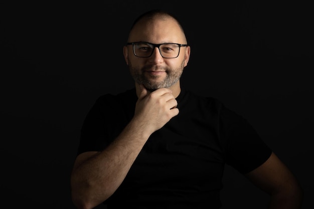 A man with glasses poses with his hand under his chin looking at the camera