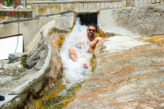 Pamukkale.Turkey에서 안경을 쓴 남자가 온천수가 있는 치유수 폭포 아래에 앉아 있습니다.