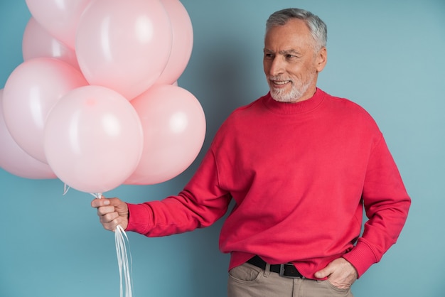 Man with gray hair and beard is holding pink balloons. Smiling man posing  , looking away