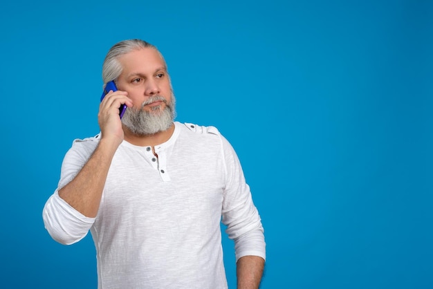 Man with gray hair and beard talking on the phone Blue background