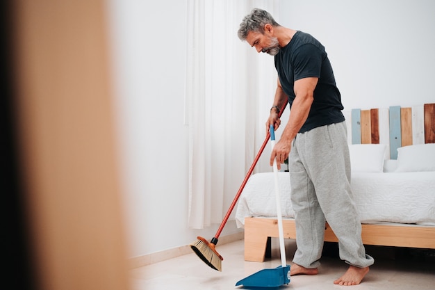 Man with gray hair in his 50s sweeping the room of his house