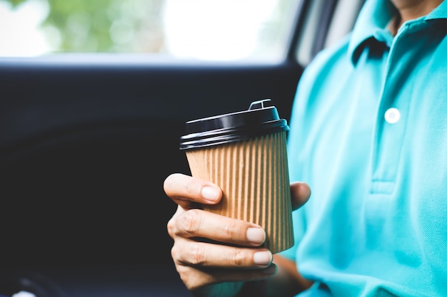 車の中で一杯のコーヒーを保持している緑のシャツを持つ男。