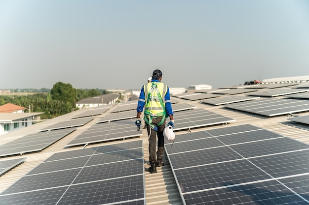 A man with a green vest walks on a roof of a building with solar panels.