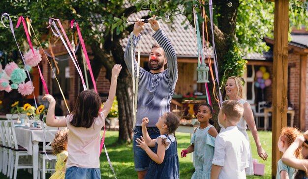 Man with group of kids on birthday party playing outdoors in
garden in summer, celebration concept.