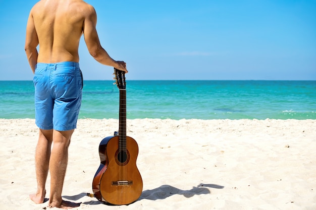 Фото Человек с гитарой на пляже с морем в качестве фона.