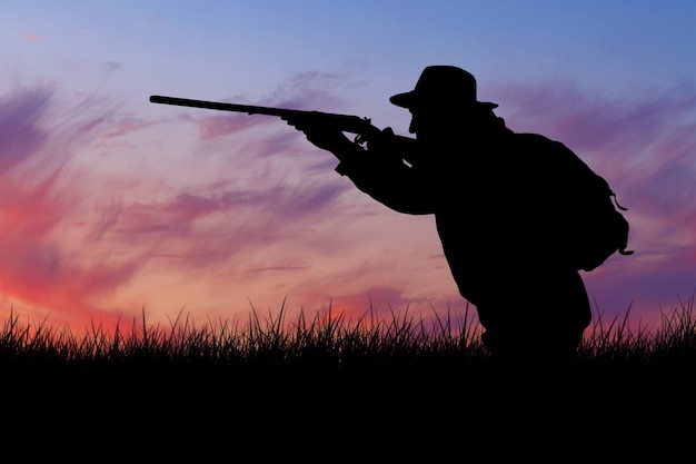 A man with a gun in his hands and an green vest on a pheasant hunt in a wooded area