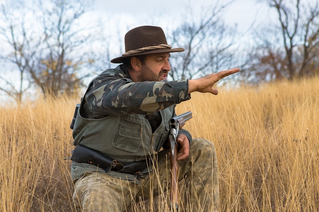 Foto un uomo con una pistola in mano e un giubbotto verde a caccia di fagiani in una zona boschiva