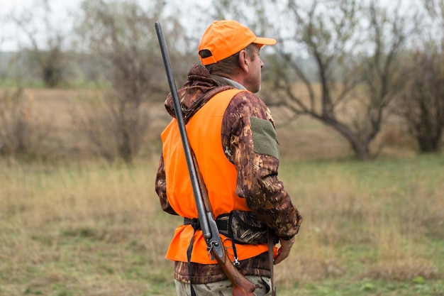 A man with a gun in his hands and an orange vest on a pheasant hunt in a wooded area in cloudy weather Hunter with dogs in search of game