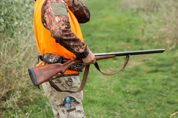 A man with a gun in his hands and an orange vest on a pheasant hunt in a wooded area in cloudy weather Hunter with dogs in search of game