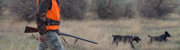 Мужчина с ружьем в руках и оранжевым жилетом на охоте на фазана в лесистой местности в пасмурную погоду Охотник с собаками в поисках дичи