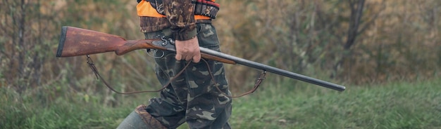 A man with a gun in his hands and an orange vest on a pheasant hunt in a wooded area in cloudy weather Hunter with dogs in search of game