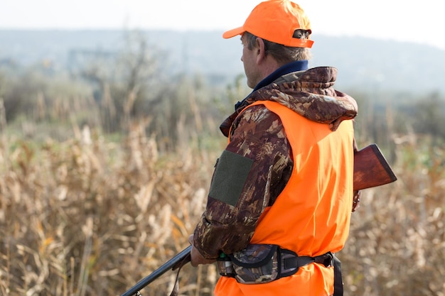 A man with a gun in his hands and an orange vest on a pheasant hunt in a wooded area in cloudy weather Hunter with dogs in search of game