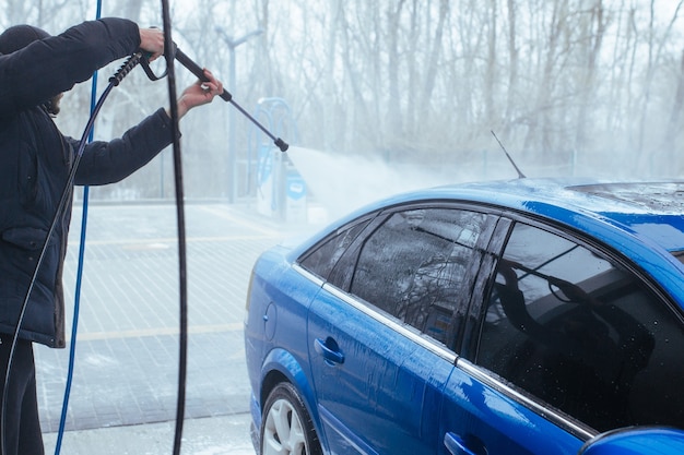 Un uomo con una pistola lava l'auto. autolavaggio self-service