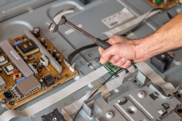 A man with a hammer and a wrench in his hands is in front of the TV, which shows the settings table