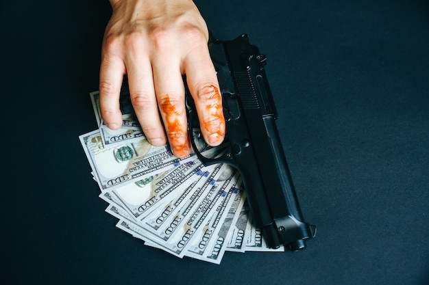 L'uomo con la mano nel sangue tiene in mano una pistola. soldi illeciti sul tavolo. dollari rubati. concetto criminale assassino.