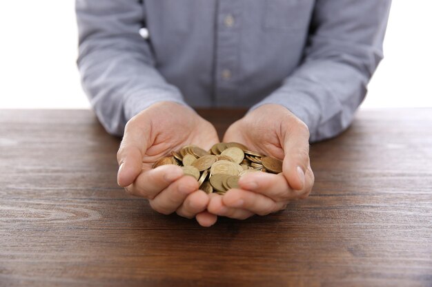 Man with handful of Ukrainian coins at wooden table on white background