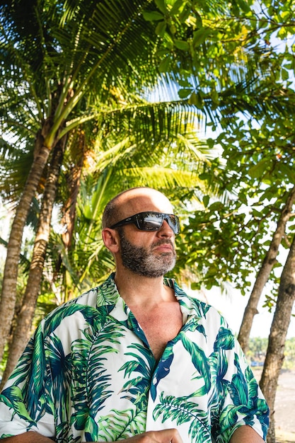 Foto uomo con una camicia hawaiana accanto alla palma