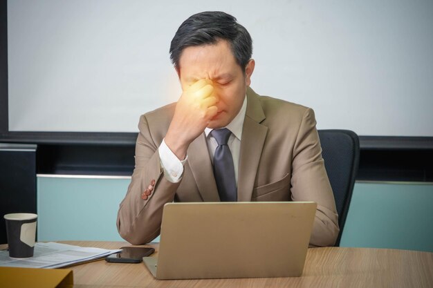 Foto un uomo con mal di testa è seduto a una scrivania con un computer portatile.