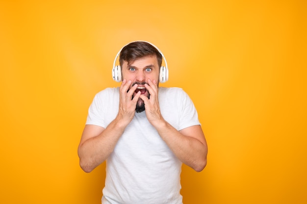 A man with headphones listening to music grabbed his mouth and demonstrates horror.