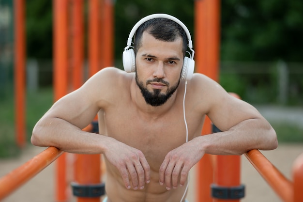 A man with headphones rests after doing push UPS on the bars outside in the afternoon