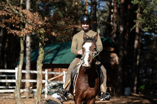 森の中で馬に乗るヘルメットを持つ男