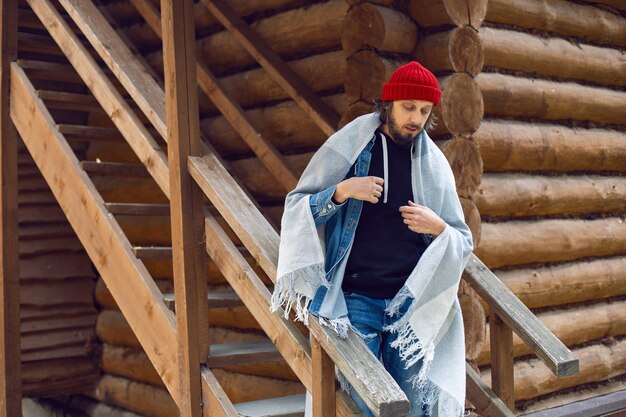 Man with a hipster beard in a red knitted hat and a denim jacket is sitting on the stairs