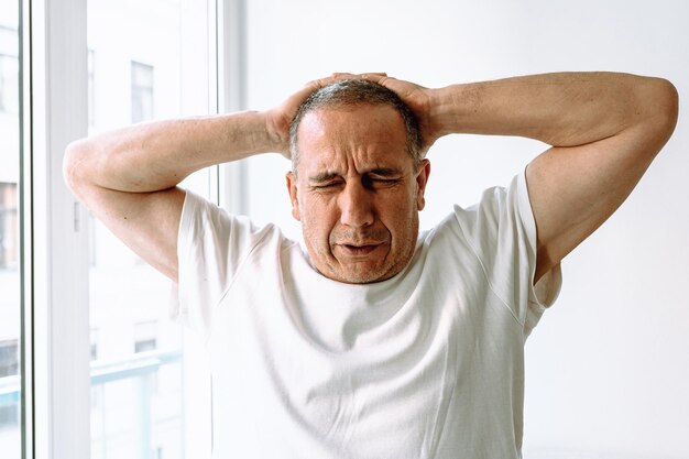 A man with his hands on his head is stretching in front of a window.