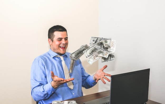 Man with his salary. office worker throwing dollars. happy face\
of top manager. guy in smart shirt and tie at the desk with\
laptop.