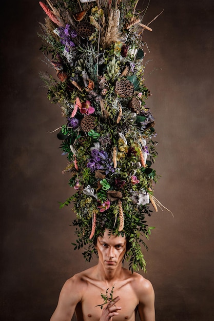 Мужчина с огромным удлиненным головным убором из живой разнообразной растительности и цветов Дитя природы сказочное существо Арт-объект