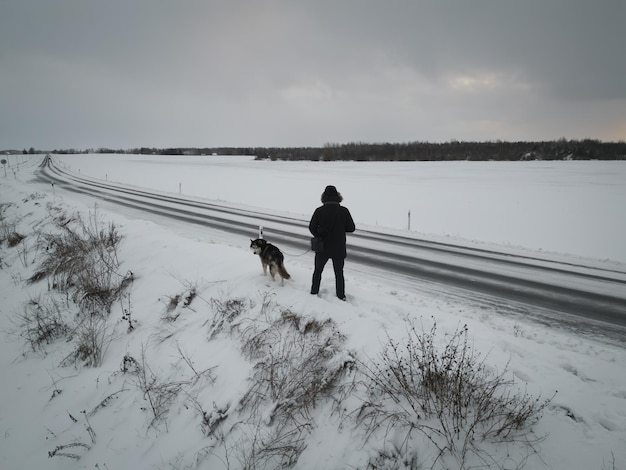 A man with a husky dog walks outdoors in winter