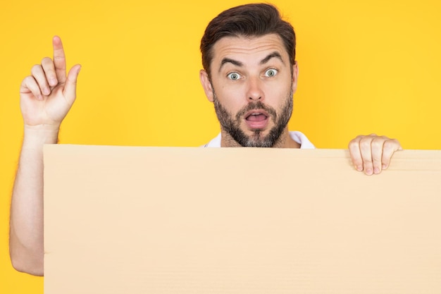 Man with idea hold blank banner ad posing isolated on studio background Portrait of attractive man holding empty blank poster Man showing blank poster pointing index up Male presenting banner