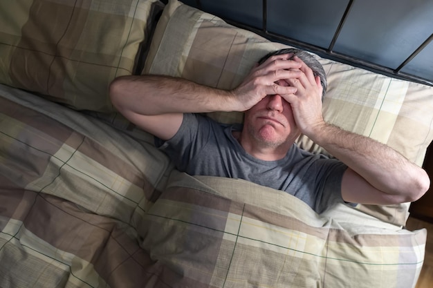 Photo man with insomnia lying in bed and snorting from exhaustion