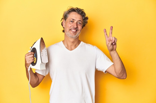 Man with iron in hand on a yellow background showing number two with fingers