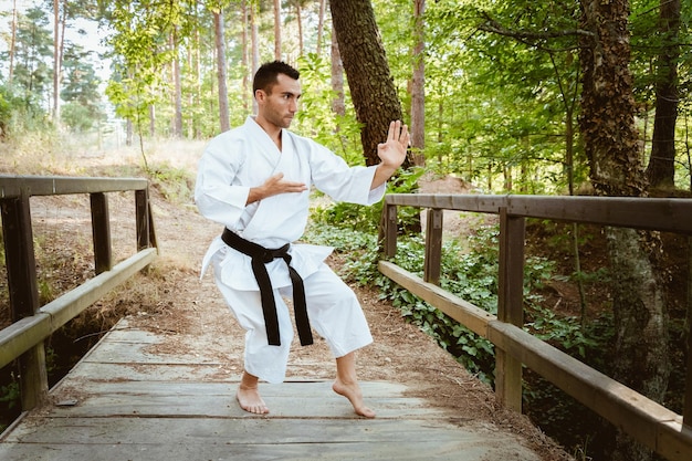 Foto uomo con karategi che pratica arti marziali nella foresta