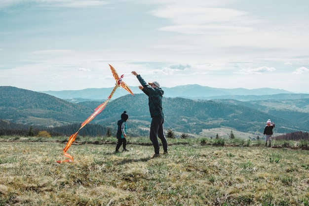 Man with kids playing outdoors with kite catching wind having fun