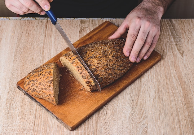 A man with a knife cuts bread on a wooden board.