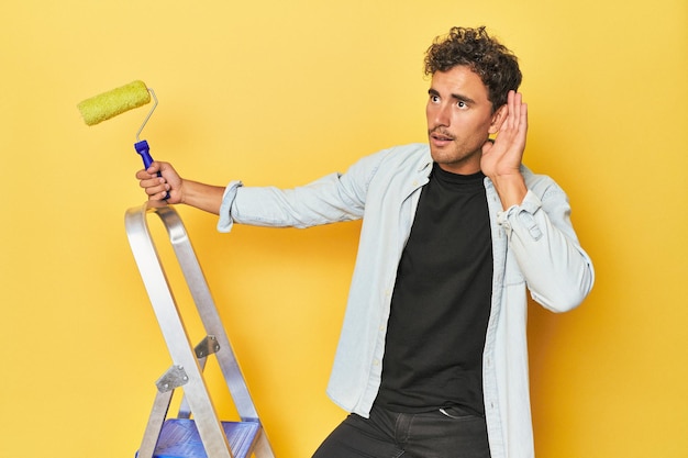 Photo man with ladder and paint roller on yellow trying to listening a gossip