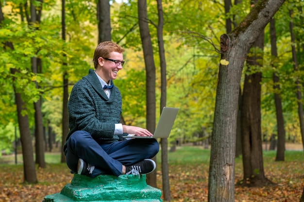 Un uomo con la parte superiore del laptop su un piedistallo che finge di essere una statua nel parco d'autunno