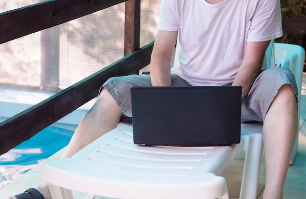 Photo a man with a laptop by the pool close-up.