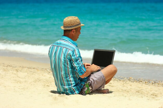 Man with laptop by the sea in summer remote work concept