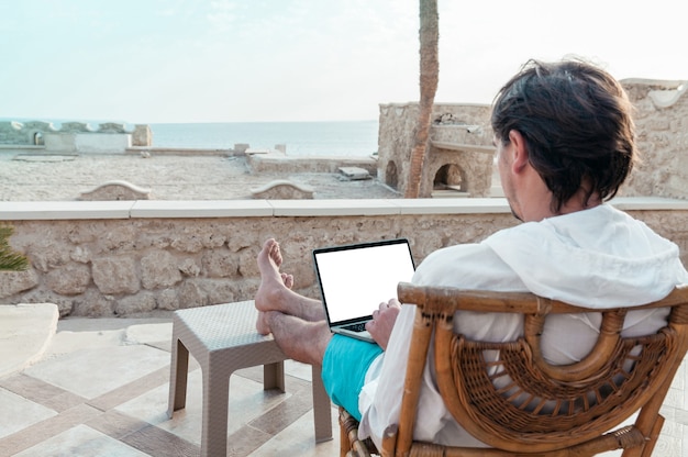 Uomo con un laptop in mano che riposa e lavora come libero professionista in vacanza