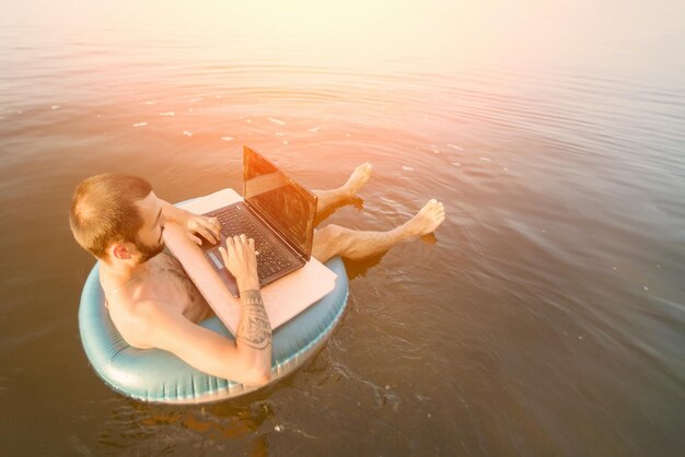 Photo man with a laptop on inflatable ring in the water