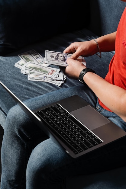 Foto l'uomo con il laptop conta i dollari in contanti e vince la scommessa online il vincitore nel casinò online conta i soldi vinti