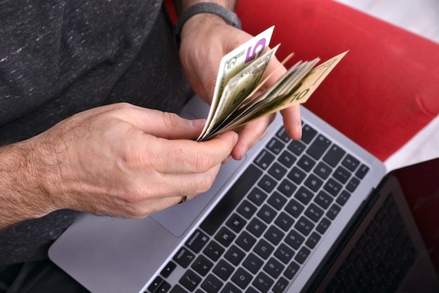 Man with laptop on lap and money in hands closeup online\
business concept