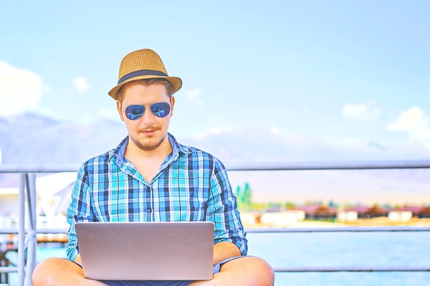 Man with laptop running remotely on colorful beach of island, on the piers.