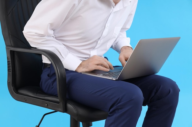 Man with laptop sitting on chair on blue background. Hemorrhoids concept