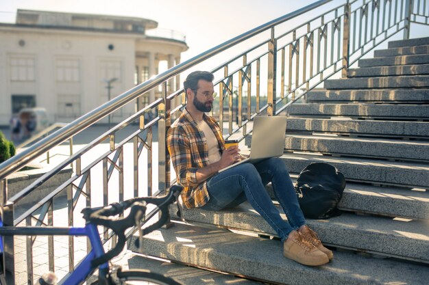 Photo man with a laptop sitting on the stairs