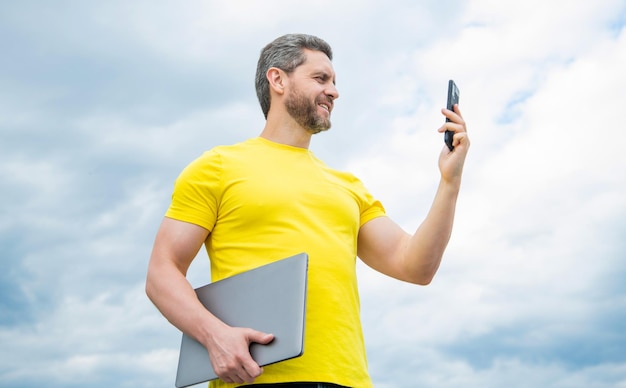 Человек с ноутбуком с помощью смартфона на фоне неба