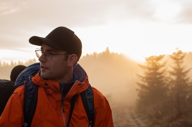 a man with a large tourist backpack at sunrise against the backdrop of mountains and forests landsca